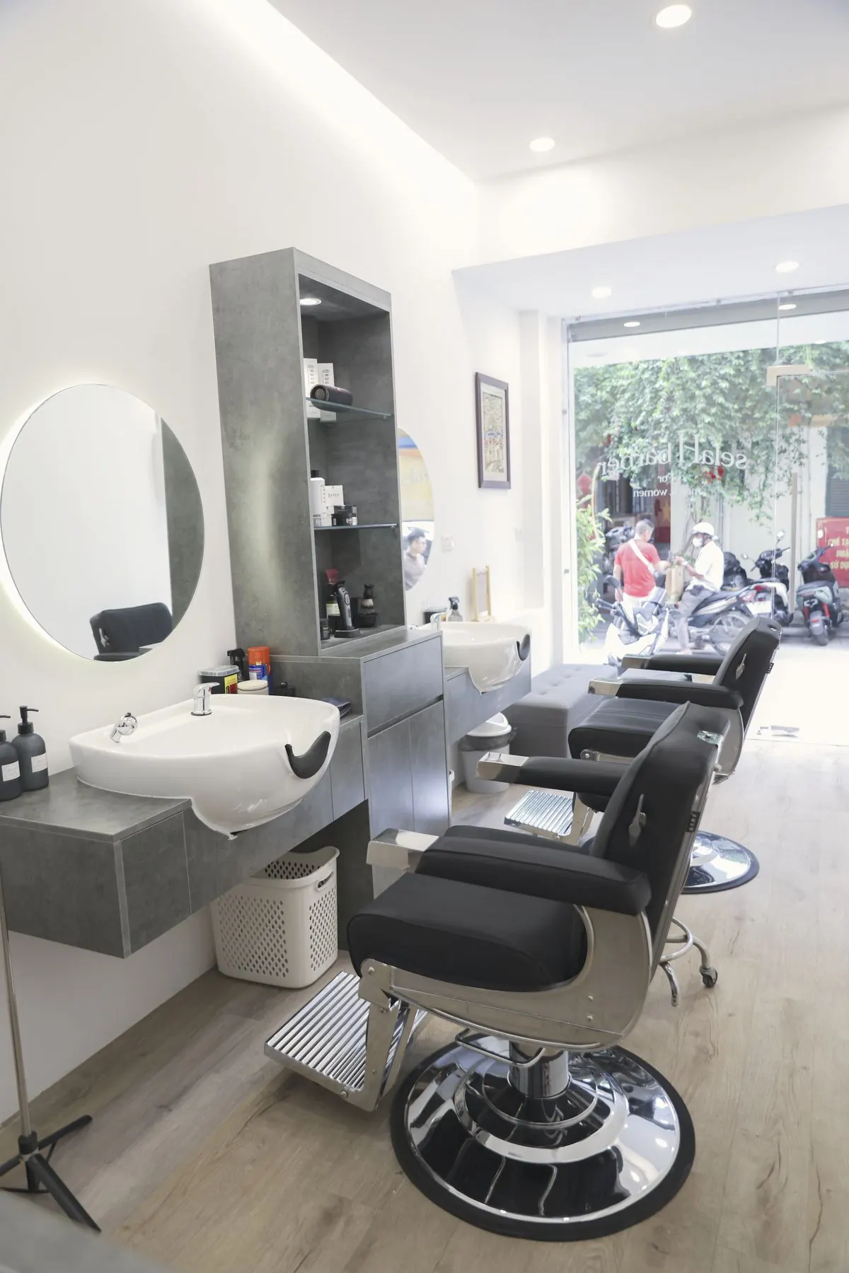 Dãy ghế cắt tóc trước gương tròn trong không gian sáng của tiệm